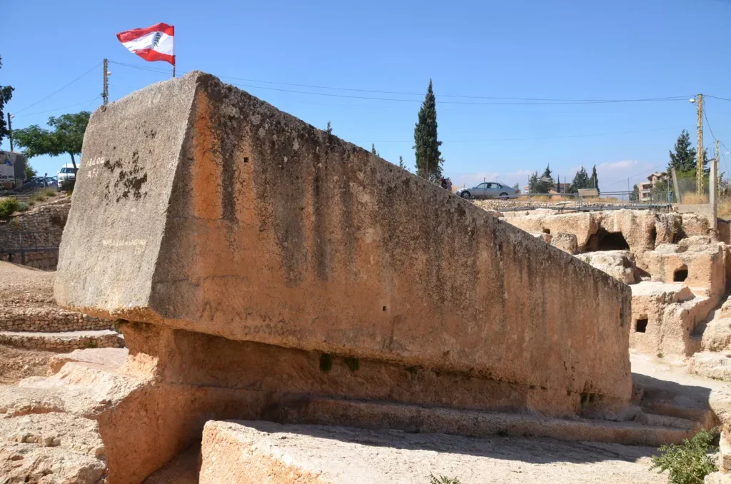 The enormous Stone of the Pregnant Woman resting at a steep angle in the Baalbek quarry, with a small Lebanese flag planted on top against a clear sky