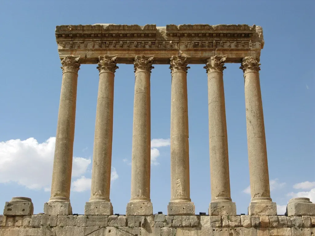 Six towering Corinthian columns with ornate entablature of the Temple of Jupiter at Baalbek, standing against a clear blue sky